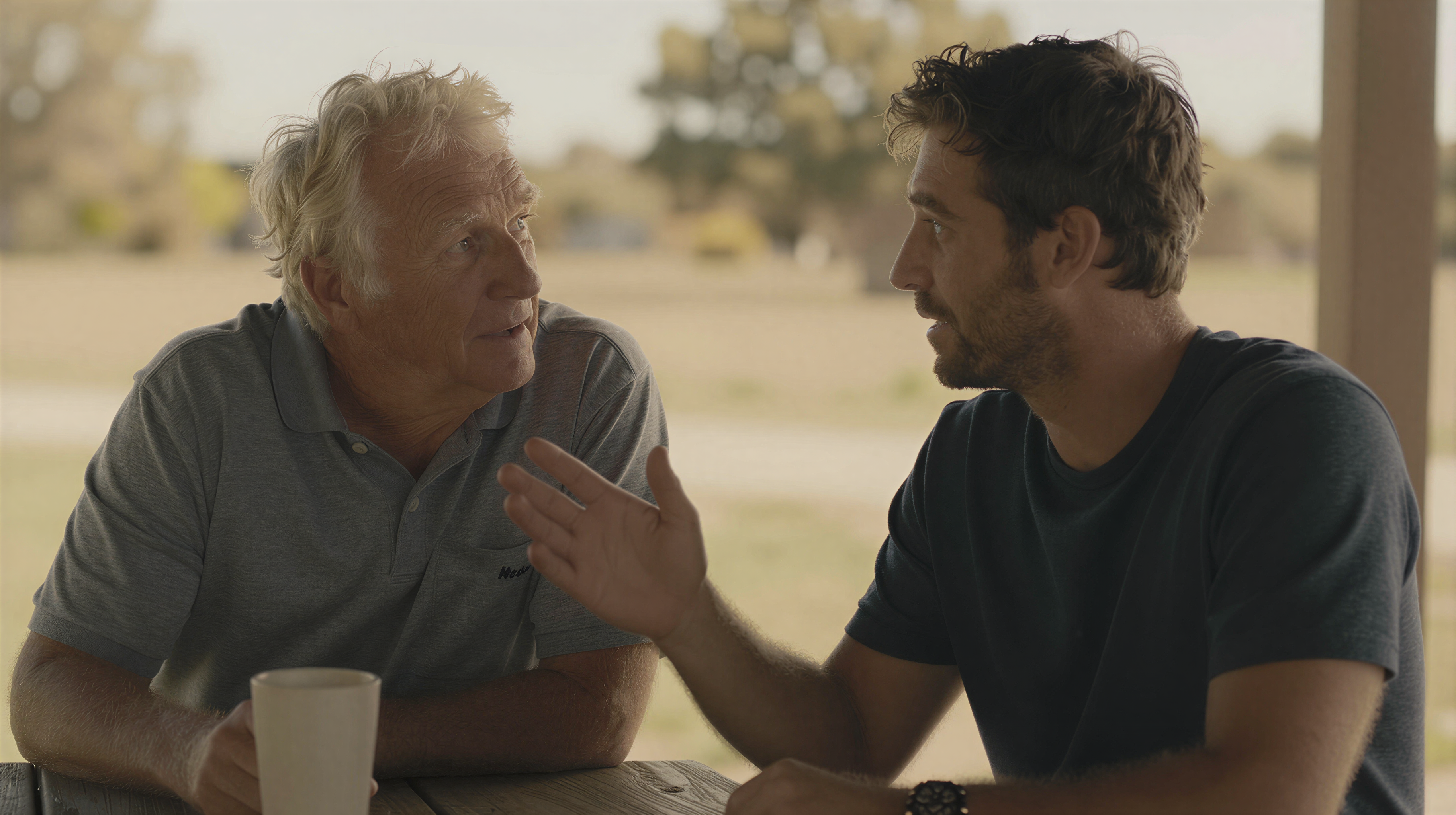 Adult son and elderly father talking outdoors in golden light